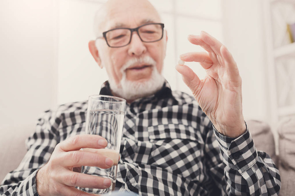 Старий має склянку води і таблетки в руці
 - Фото, зображення