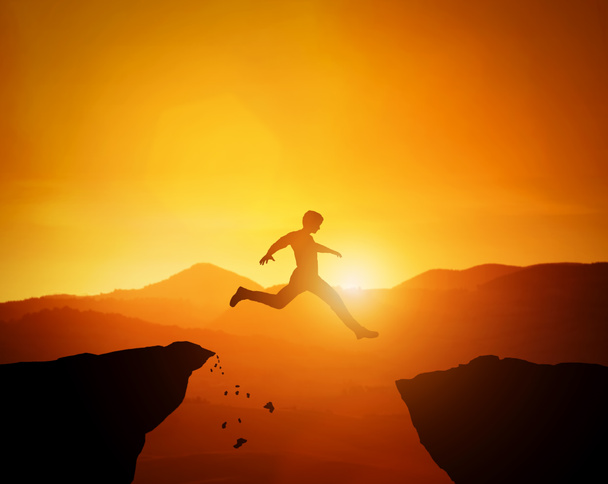 Um homem saltando de uma rocha para outra. Sunset montanhas paisagem
 - Foto, Imagem