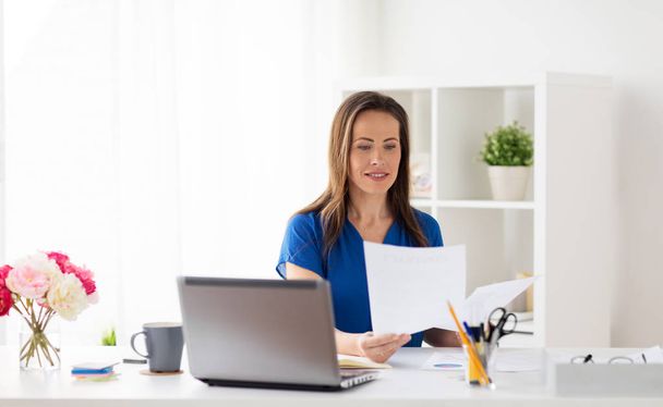 happy woman with papers and laptop at office - Valokuva, kuva