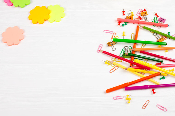 Colorful pencils and felt-tip pens, color notepaper, paper clips, stationery nails on white wooden background - Photo, Image
