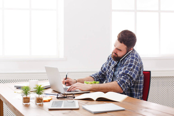 Молодий зайнятий бізнесмен з ноутбуком обідав в сучасному білому офісі
 - Фото, зображення