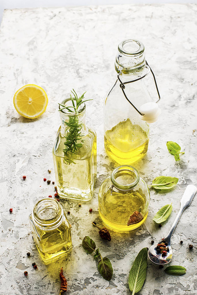 Four bottles of different sizes with vegetable oil, sunflower and olive on a light marble background with the addition of pepper, sage leaves and basil for kitchen and cosmetic use. Selective focus. - Fotografie, Obrázek