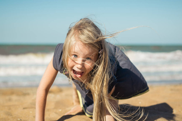 Krásná dívka v šedých šatech dělá Veselý obličej na písku u moře. - Fotografie, Obrázek
