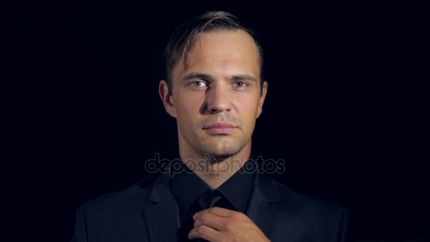 closeup of a man in black clothes on black background. 4k. Slow motion. man adjusts his tie, smiles and looks into the camera - Video