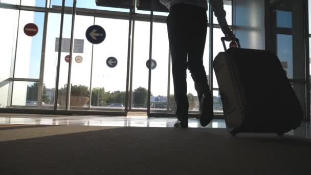 Бизнесмен, идущий из аэропорта со своим багажом. Человек, выходящий через стеклянную автоматическую дверь на улицу и катающий чемодан на колесах. Солнечная вспышка на заднем плане. Концепция поездки или путешествия. Медленное движение
 - Кадры, видео