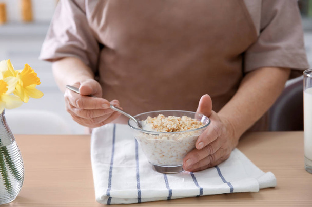 Elderly woman eating tasty oatmeal with milk  - Foto, afbeelding