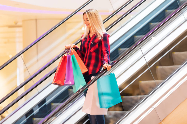 Young woman with shopping bags on escalator in the fashion store - Foto, Imagem