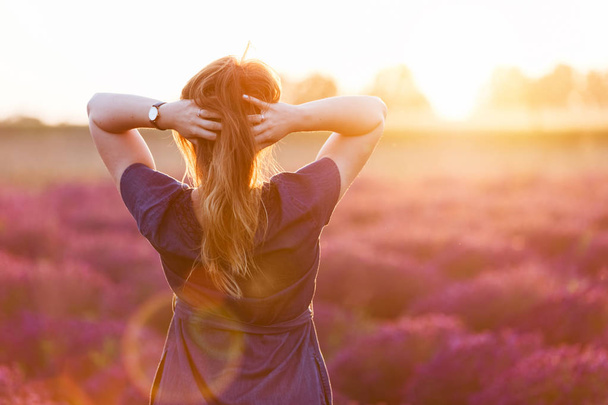 Nuori nainen koskettaa hänen pitkät hiukset katsomalla laventeli alalla
  - Valokuva, kuva