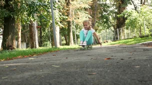 Young girl rides the skateboard in a seated position in park. Slow motion.  - Video
