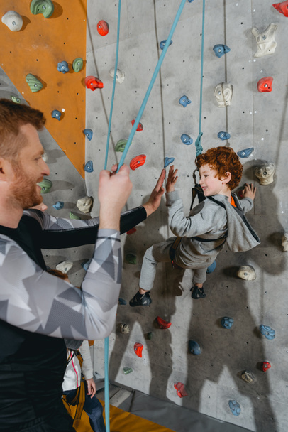 Boy on climbing wall high-fiving father - Photo, Image