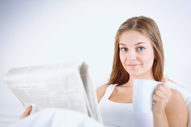 A pretty young woman reading the newspaper in bed and enjoying a cup of tea. - Φωτογραφία, εικόνα