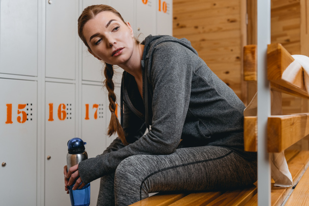 Woman sitting on bench in locker room - Foto, afbeelding