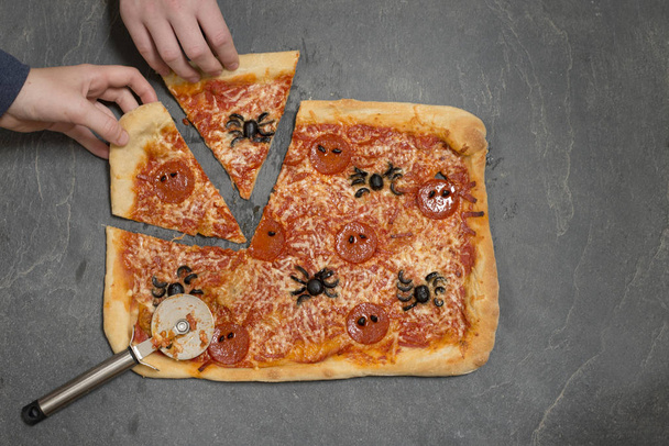 Handen oppakken van segmenten van Halloween-Themed Pizza met Pizza Cut - Foto, afbeelding
