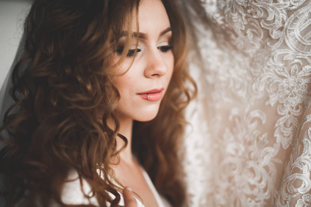 Gorgeous bride in robe posing and preparing for the wedding ceremony face in a room - 写真・画像