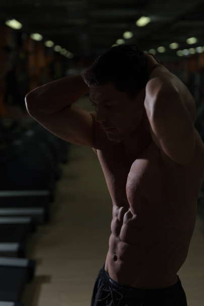 Muscular hombre entrenamiento con mancuernas en cuarto oscuro
 - Foto, imagen