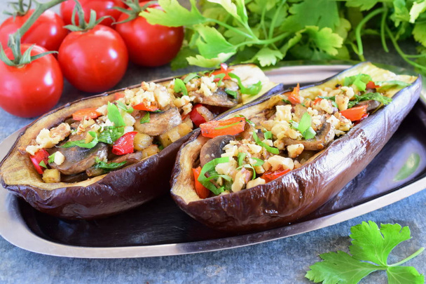 Eggplants stuffed with mushrooms, onions, carrots, tomatoes and nuts on a metal plate on a grey background. Vegetarian food. healthy eating concept. - Photo, Image