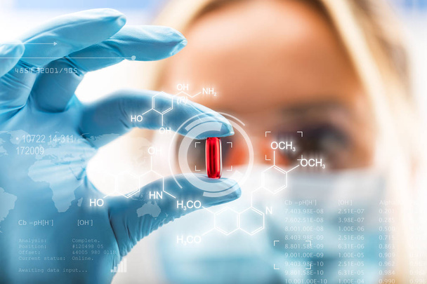 Young attractive female scientist holding a red transparent pill - Foto, Bild