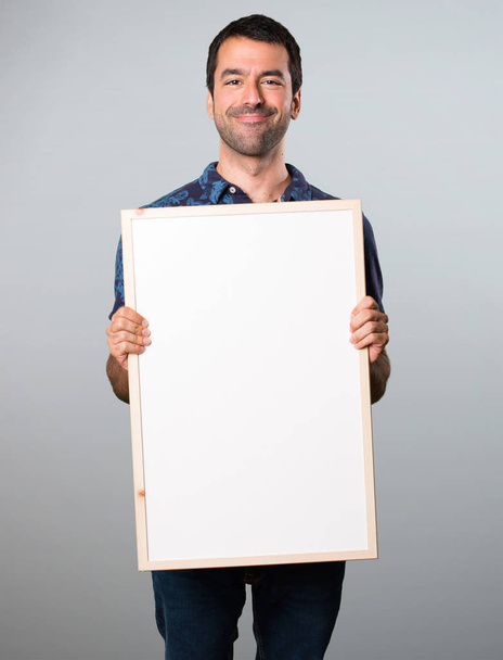 Brunette man holding an empty placard on grey background - Photo, Image