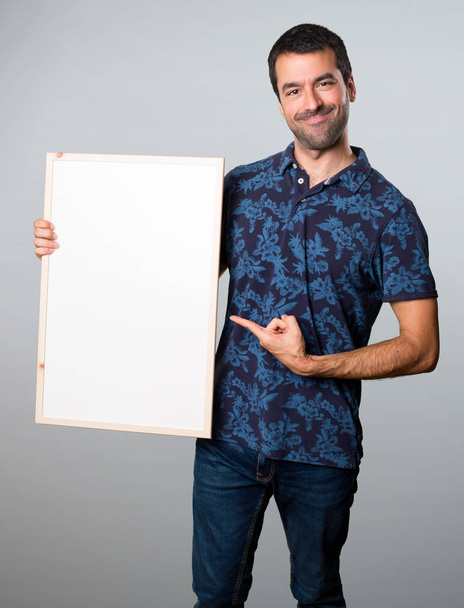 Brunette man holding an empty placard on grey background - Photo, image