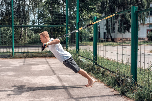 A sports person, fresh air is engaged in training training loops, in sports clothes, in summer in the city, wringing out. Strength and stamina motivation. - Zdjęcie, obraz