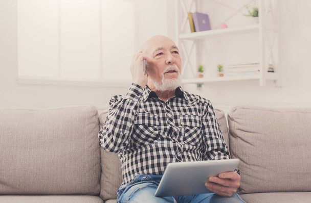 Vanhempi mies puhuu puhelimessa tabletin kanssa
 - Valokuva, kuva
