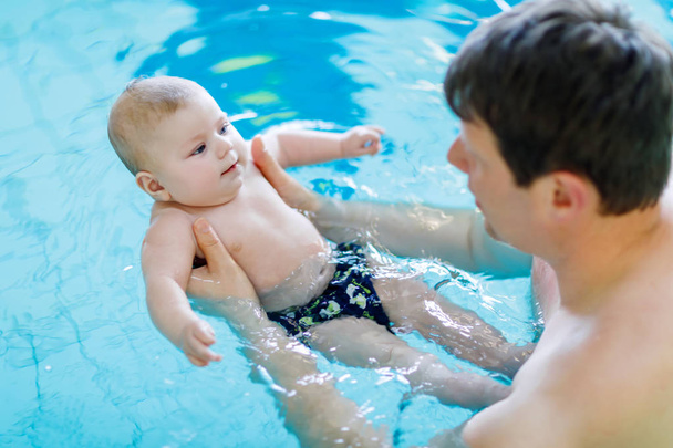 Happy middle-aged father swimming with cute adorable baby in swimming pool. - Photo, image