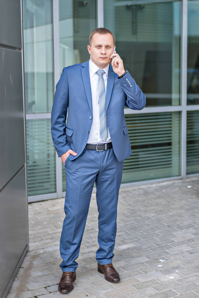 portrait of a young serious businessman in blue suit talking holding phone - Foto, Bild