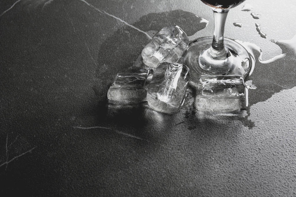 Διαρροή νερού από γυαλί νερού με πάγο σε σκούρο τραπέζι. - Φωτογραφία, εικόνα