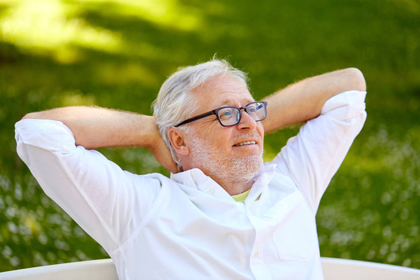happy senior man in glasses sitting at summer park - Photo, image