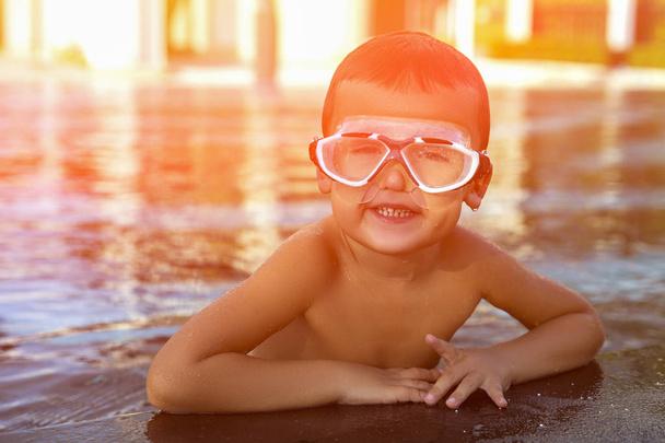 Um menino feliz relaxando ao lado de uma piscina usando óculos de proteção. Tonificado
 - Foto, Imagem