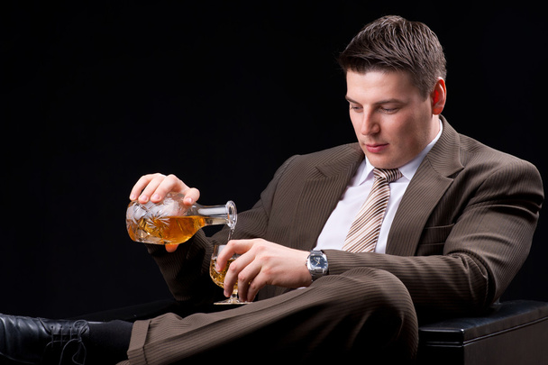 Young businessman sitting on a couch with an alcoholic beverage - Фото, зображення