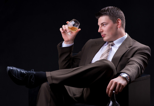 νέος επιχειρηματίας που κάθεται σε έναν καναπέ με ένα αλκοολούχο ποτό - Φωτογραφία, εικόνα