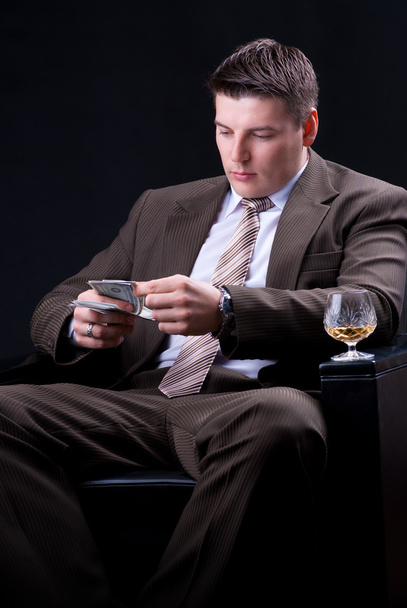 Young businessman with money and an alcoholic beverage sitting in the chair - Foto, immagini