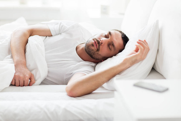 man sleeping in bed with smartphone on nightstand - Zdjęcie, obraz