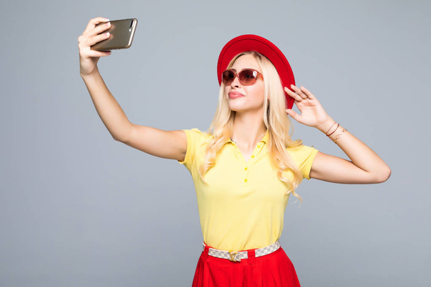 Trendy beautiful hipster girl taking selfie with mobile phone agains gray - Foto, afbeelding