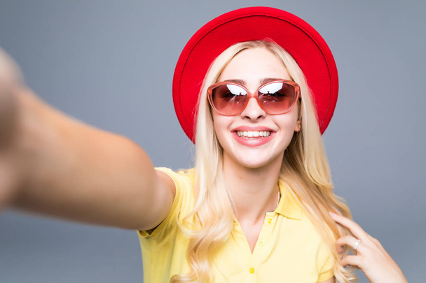 krásná šťastná usmívající se sexy blond žena pěkná ležérní letní barevné šaty s červenými rty izolované na šedém provedení selfie foto na smartphone - Fotografie, Obrázek