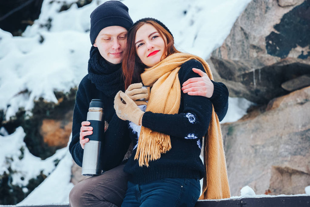 Young couple pours hot tea out of thermos in winter forest - Photo, Image