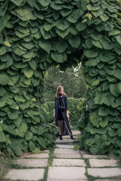 Дівчина стоїть в чорній довгій сукні під аркою
  - Фото, зображення