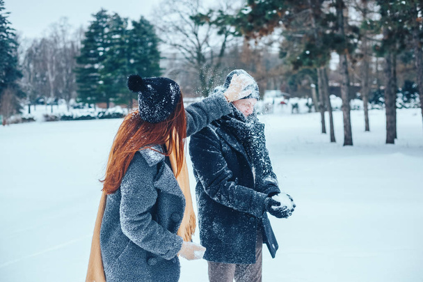 Ο τύπος και το κορίτσι ξεκουράζονται στο δάσος του χειμώνα. Σύζυγοι στο χιόνι. Νεαρό ζευγάρι με τα πόδια στο πάρκο το χειμώνα. - Φωτογραφία, εικόνα