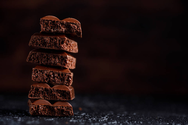 Porous chocolate in stack on a black background closeup. Pieces of milk porous chocolate, lying on top of each other. Place under your text. - Foto, Bild