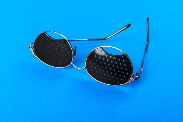 zwei verschiedene Brillentypen auf blauem Hintergrund. Medizinkonzept. Ansicht von oben. Lochblende schwarze Brillen helfen müde Augen zu entspannen, die auf weißem Hintergrund isoliert sind. Optische Brillen in klassischer Mode. - Foto, Bild