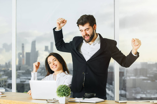 Portrait of attractive man and woman working together at modern office desk and celebrating success. Successful concept - Фото, изображение