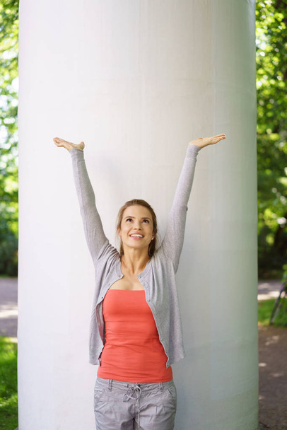 Young woman standing by column with raised arms - Foto, Bild