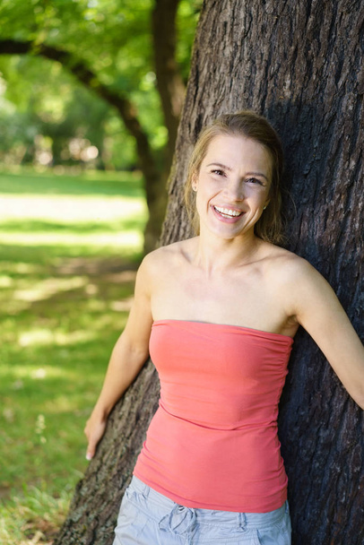 Young woman leaning against tree in park - Foto, immagini