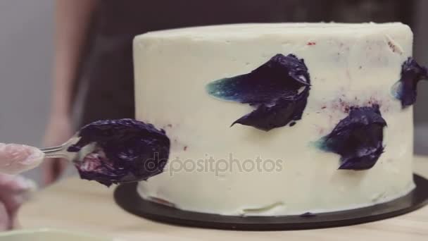 Рука пекаря-десерта размазывает фиолетовый крем на белой глазури
 - Кадры, видео