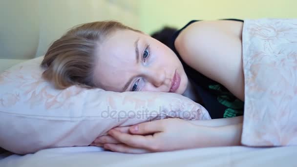 Mujer joven con ojos azules acostada en la cama después de despertarse temprano en la mañana
 - Imágenes, Vídeo