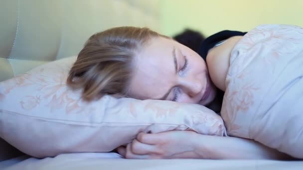 Mujer joven con ojos azules bosteza en la cama después de despertarse temprano en la mañana
 - Imágenes, Vídeo
