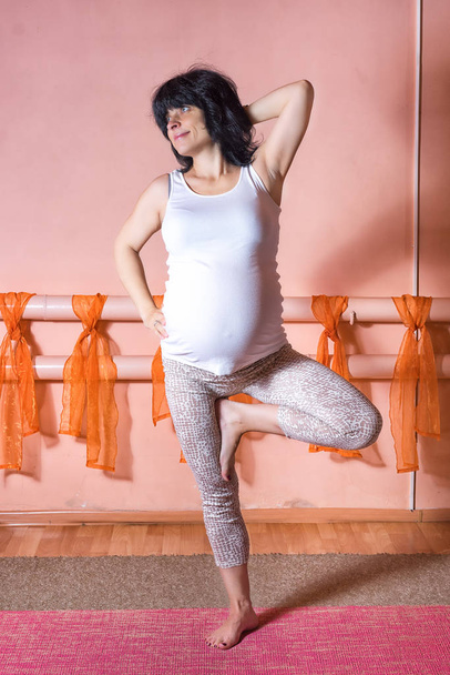 Schwangerschaftsyoga und Fitnesskonzept. gesunder Lebensstil Mutterschaft Konzept. 40 Wochen schwangere Kaukasierin mittleren Alters steht auf einem Bein in Gomukasana Asana. - Foto, Bild