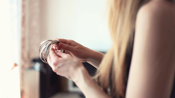 Νεαρή ξανθιά γυναίκα βάζει στοίβα βραχιόλια βραχίονα στο σαλόνι - Πλάνα, βίντεο