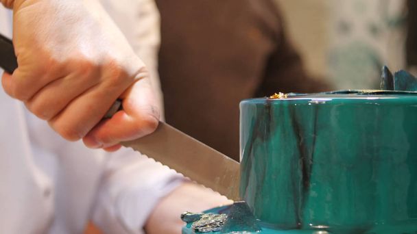 Der Konditor schneidet den Kuchen mit einem langen Messer an. einen türkisfarbenen Kuchen anschneiden. der Konditor schneidet den Kuchen an - Foto, Bild